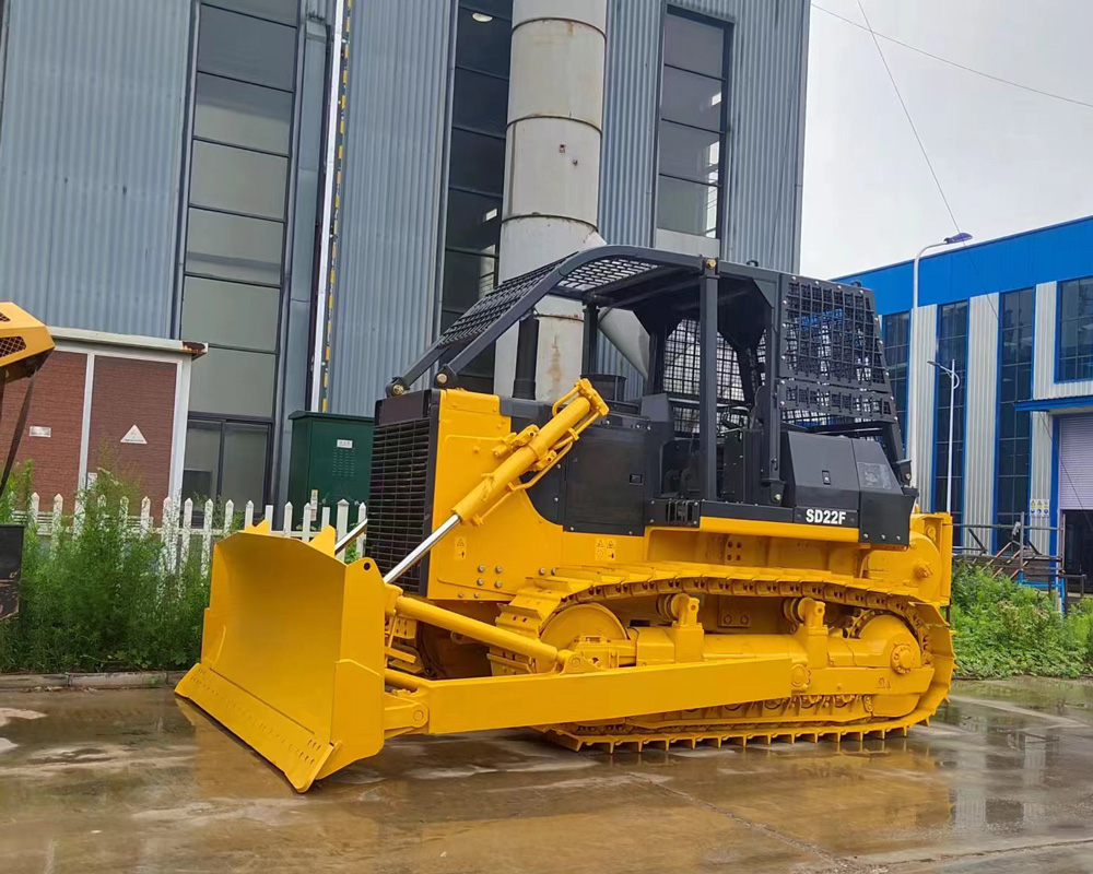 SHANBO SD22F crawler bulldozer staged outside the SHANBO Shandong factory yard — industrial warehouse facade backdrop