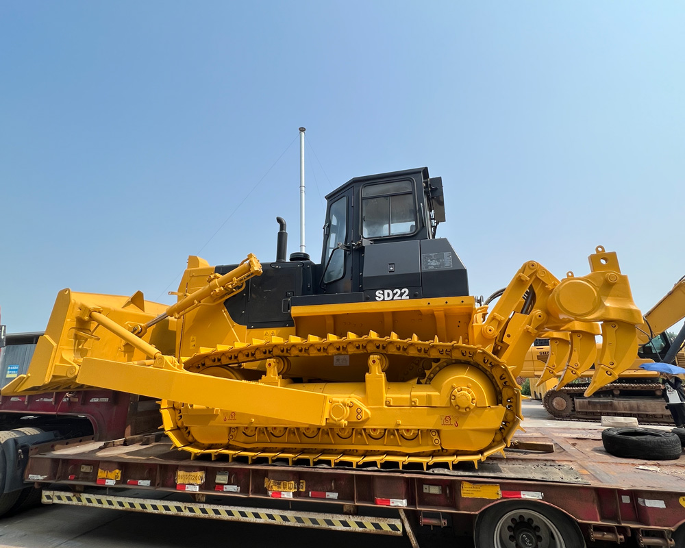 SHANBO SD22 محمل على مقطورة مسطحة لشحن التصدير — تسمية الطراز مرئية على الكابينة، سماء مشرقة في الخلفية